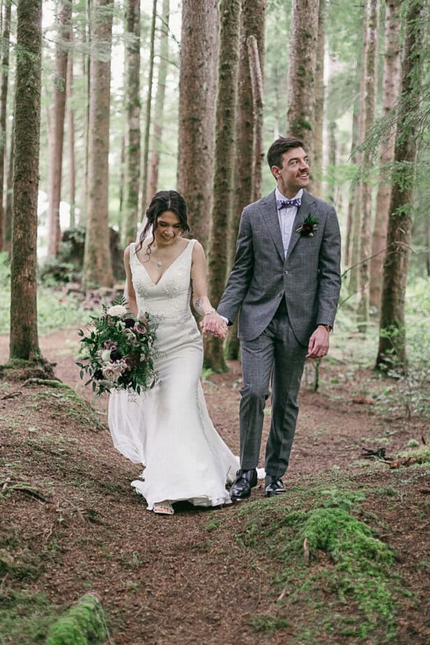 Bride and groom walk hand in hand in the forest in Forks, Washington.