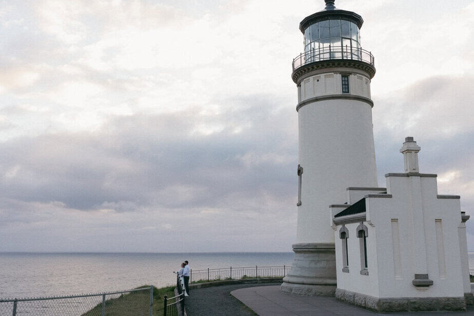 Bride and groom stand next to a lighthouse in Cape Disappointment. 