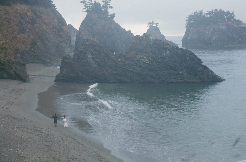 Bride and groom walk along the beach in the rain in Brookings, Oregon.