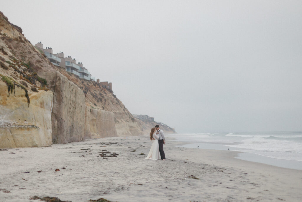 An elopement couple hold hands as they walk on the beach in San Diego, California,