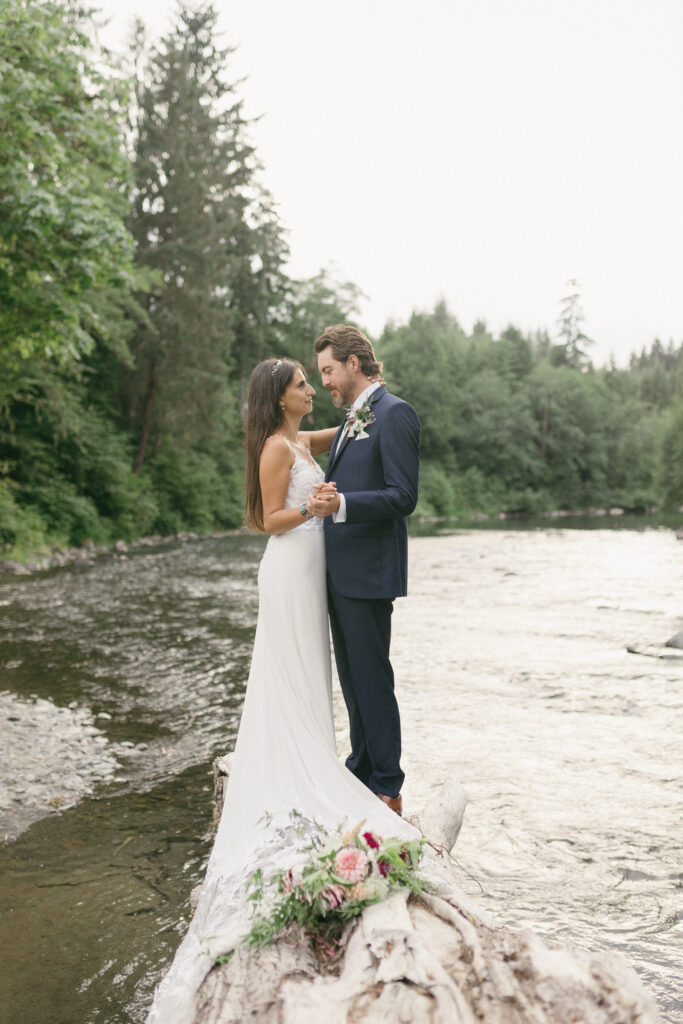 Bride and groom stand on a log along the Hoh River in Forks, Washington.